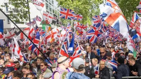 EPA/Shutterstock Crowds gather behind a barrier waving a selection of flags