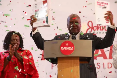 AFP John Mahama (R), holds a copy of the party's manifesto as his running mate Jane Naana Opoku-Agyemang (L), looks on in Winneba, Ghana, on August 24, 2024