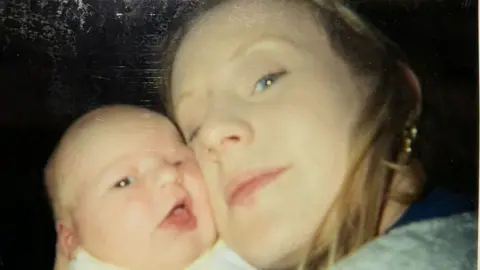 Sabrina Lyttle, then in her early 20s and with blonde hair and a gold earring, poses for a picture with her right cheek pressed against the cheek of her baby daughter