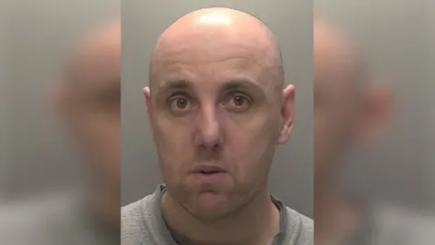 Police custody photograph of David Brennan who is bald and is wearing a grey top