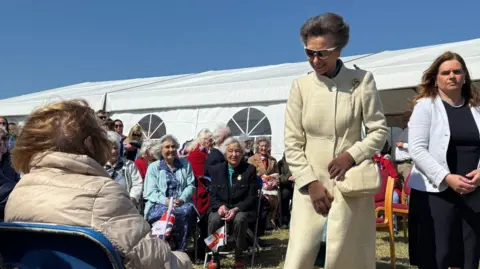 The Princess Royal in a cream coat meets members of the public in front of a marquee.
