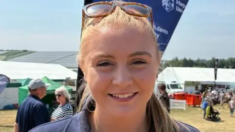 A woman with blond hair smiles as her sunglasses sit on the top of her head.