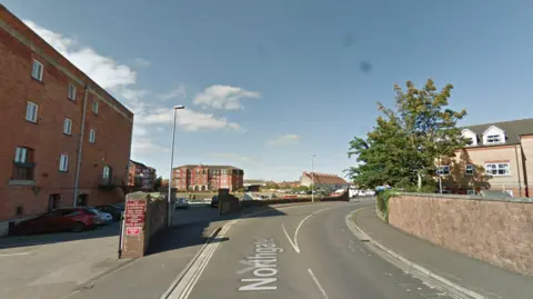 A road with houses on both sides. It is sunny and the sky is blue.