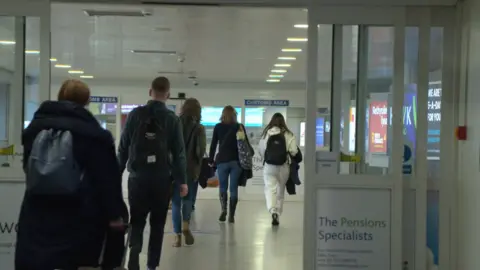 Passengers walking through automatic doors in Jersey airport towards the customs area.