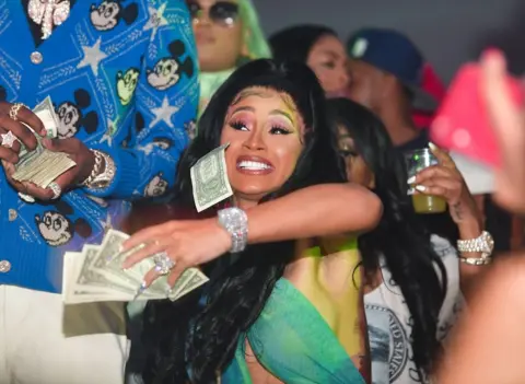 Getty Images Cardi B throws a handful of dollar bills into a crowd during a party in 2020