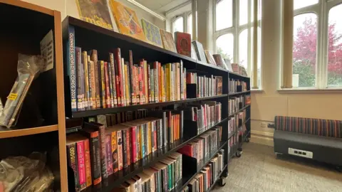 A bookshelf with books on four levels of shelving and on top