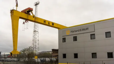 位於貝爾法斯特的 Harland & Wolff 集團控股造船廠入口附近，標誌性的 Harland & Wolff Samson 和 Goliath 黃色龍門起重機之一。天空多雲。