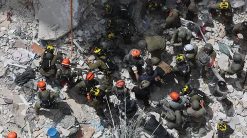 EPA Members of Israel's Home Front Command search for missing people under the rubble of a partially collapsed residential building