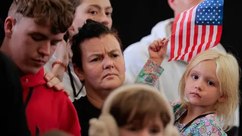 Getty Images White Afrikaners, who are mostly descendants of Dutch and French settlers, are seen being welcomed to the US as one holds up a US flag