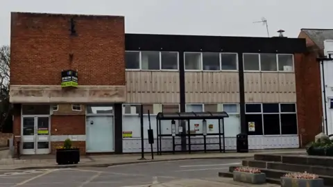 Jennifer Lawler/The March Society A two storey 1970s building of brick and concrete cladding on a street, with a bus shelter outside.