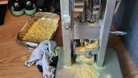 Crown Prosecution Service Aluminium baking tray full of pills next to aluminium machine with yellow powder scattered over the bottom