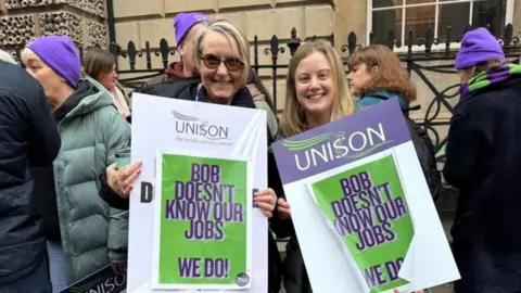 BANES Unison branch Two female protesters hold up Unison placards that read: 'Bob doesn't know our jobs, we do!'