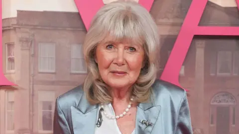 PA Dame Jilly Cooper astatine  the premiere of Rivals lasting  against a poster for the Disney+ series.