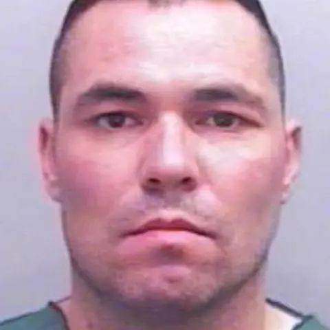 Devon and Cornwall Police Police mugshot of Shane Jenkin following his arrest. He has a stern look on his face is has stubble.