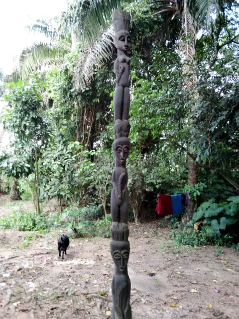 Abiodun Omotoso Uma longa escultura em madeira é vista na borda de um grupo de árvores