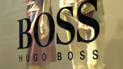 A Hugo Boss shop window in close up. There are two mannequins in the background and the words Boss, Hugo Boss are emblazoned across the window in black type. 