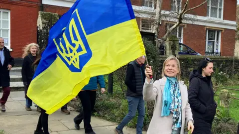 Jon Wright/BBC A woman waves a Ukrainian flag as she walks towards a church