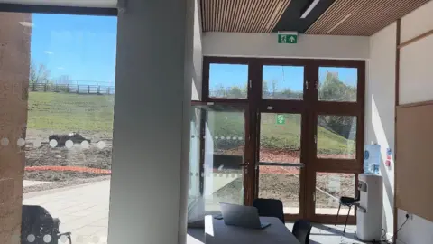 LDRS Inside the visitor centre. There is a table for a laptop on and some windows in the background. 