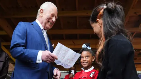 The King laughs while holding a sheet of paper in his hand while meeting a woman and child at the Harlem Grown community initiative in Upper Manhattan on Wednesday.
