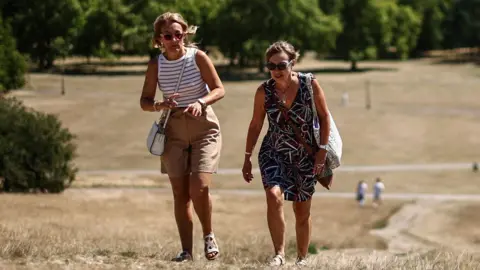 Two women walk across parched brown grass in the sunshine