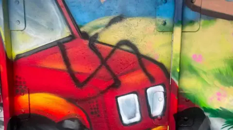 Declan Norris A swastika symbol in black spray paint is seen on a mural, which includes a red tractor and field