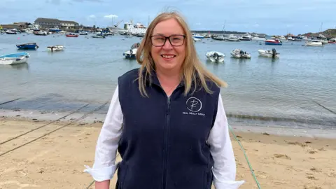 Lisa Farrington-Martin standing in front of a strip of beach and a body of water with many anchored boats in the background.