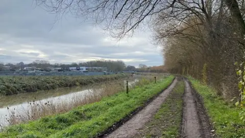 Plamena Naydenova A mud track runs alongside a rive. It is shelted by a high hedgerow, has no lights and looks gloomy.