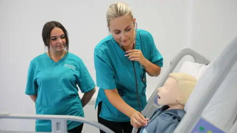 Students dressed in scrubs testing out the new realistic hospital equipment on a mannequin patient