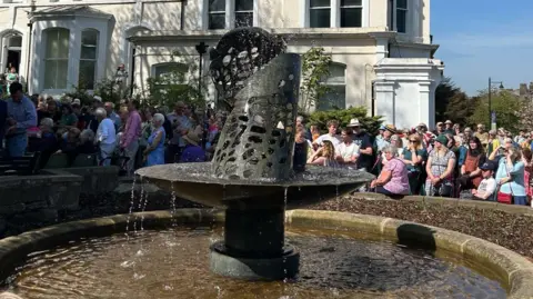 A fountain with lots of people surrounding it on a sunny day.