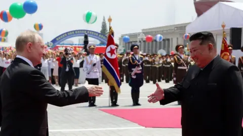 EPA Mr Putin and Mr Kim smile and reach out towards each other to shake hands, with a parade in the background