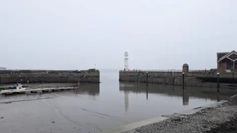 A grey sky reflects down onto grey water at Newhaven Harbour.