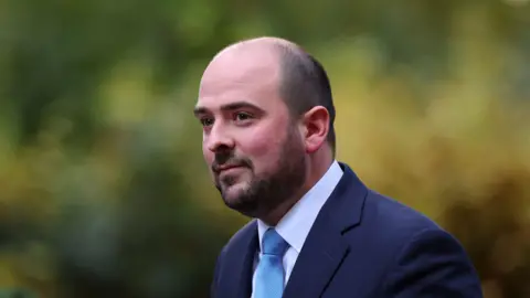 Toby Melville/Reuters A head-and-shoulders picture of MP Richard Holden, a bald man with a dark brown beard. He is wearing a navy suit with a white shirt and blue tie.