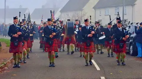 David Kerr A band of pipers march through a foggy town.