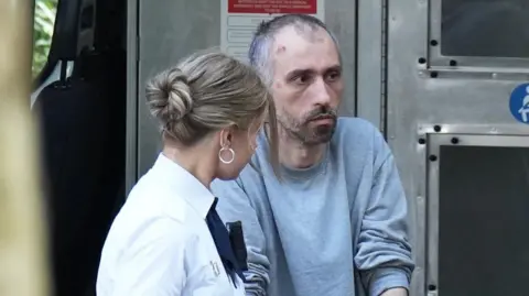 Eddie Mitchell A man is led into court. He is in grey prison clothes. 