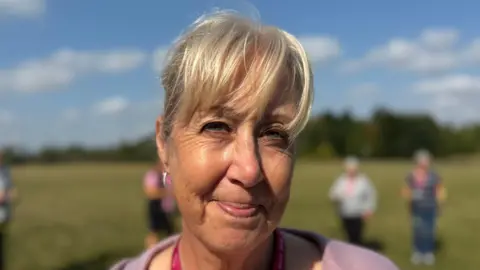 Elliot Deady/BBC A smiling Karen Brimson looks straight into the camera while standing in a field.