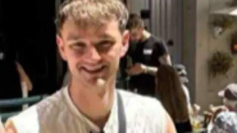 Family photo Kieran Thomas Hughes smiling into the camera. he has a short blonde hair with bangs. He is wearing a white shirt