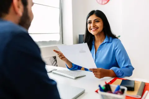 Interviewer looking at candidate while smiling and holding candidate's CV
