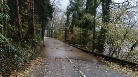 Graham Russell Photo of a flooded road with water covering the road entirely with the river to the right.