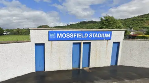 The stone entrance to a football pitch with a blue sign that reads "Mossfield Stadium" and has an Argyll and Bute Council logo.