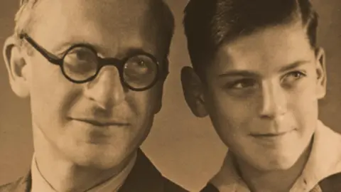 Marianne Philipps An older man wearing black spectacles, smiles and poses with a young boy