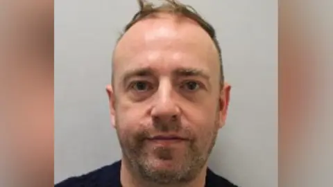 Met Police A mug shot of Gunnery who has brown hair and facial stubble and is wearing a black jumper