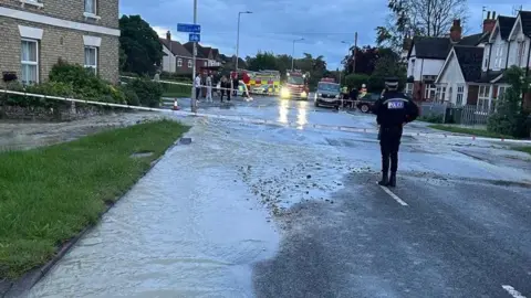 A police officer stands in front of a cordon, which has shut a flooded road