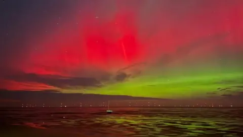Vivid pink, red and green lights are visible in the night sky above the sea