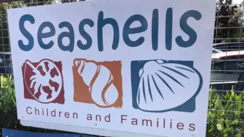 A sign for Seashells family hub in Sheerness. There is some plants in the background. 