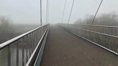 A picture of the path across a footbridge on a misty day. 