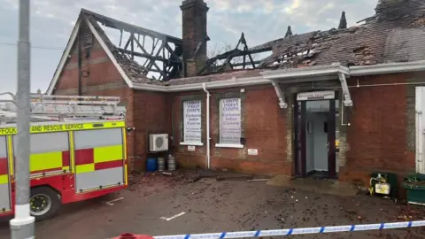 The roof of a brick building is partially burnt. In places there is just a timber shell remaining, with holes in other parts of the roof.