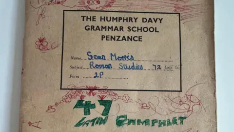 Humphry Davy School The front cover of the exercise book. It is headed 'The Humphry Davy Grammar School Penzance' and has 'Sean Morris, Roman Studies, 2P' handwritten on it. The rest of the cover has doodles in red and green pen. 