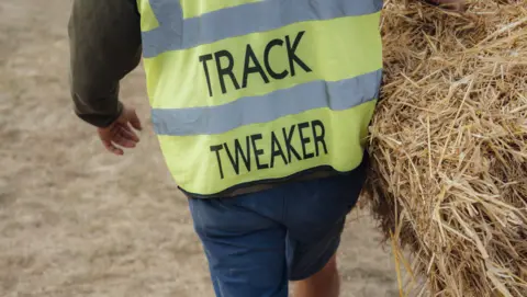 Harry George Hall Man in a high vis with the words Track Tweaker carries a bale of hay