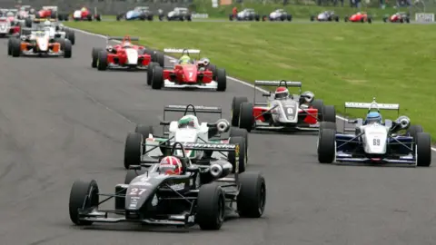 Getty Images British Formula Three Championship at Castle Combe in 2005: a view down the track with dozens of formula three cars - which look a little like less engineered formula one cars. Various colours - lots of red, white and black.