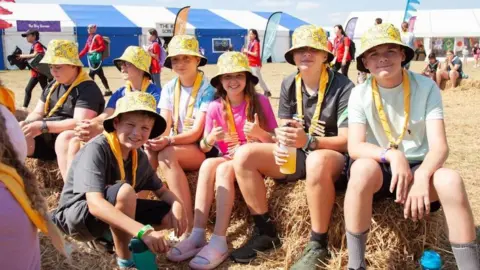 Essex Scouts A group of young scouts and guides wearing colourful bucket hats sit on hay bales